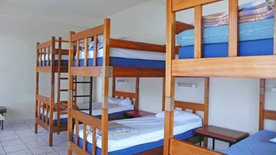 Wooden bunk beds with blue mattresses in a simple dormitory room with tiled floors.