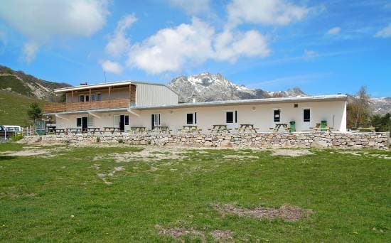 Mountain refuge with picnic tables below snow-capped peaks at Col de Vergio
