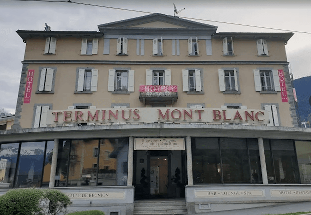 Hotel Terminus Mont Blanc building facade with "HOTEL" banners and large ground-floor windows reflecting mountains.