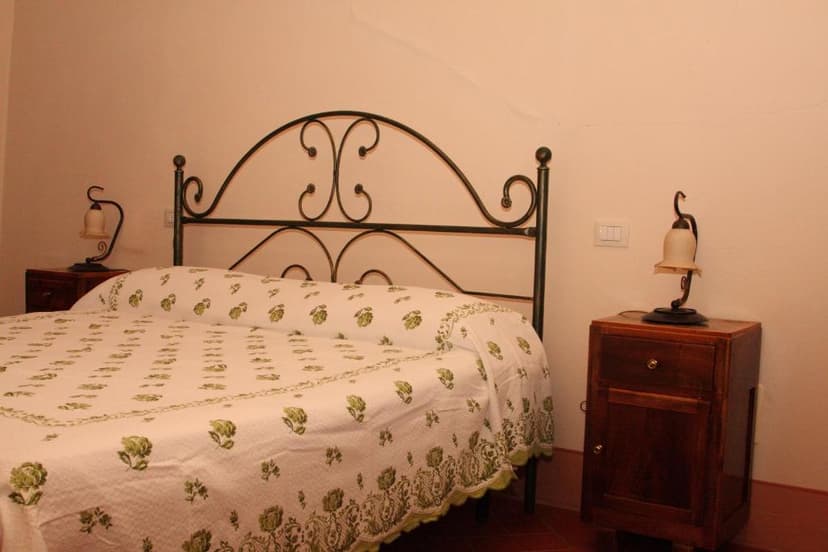 Bedroom with wrought iron bed, green floral quilt, and wooden nightstands in Villa del Cardinale.