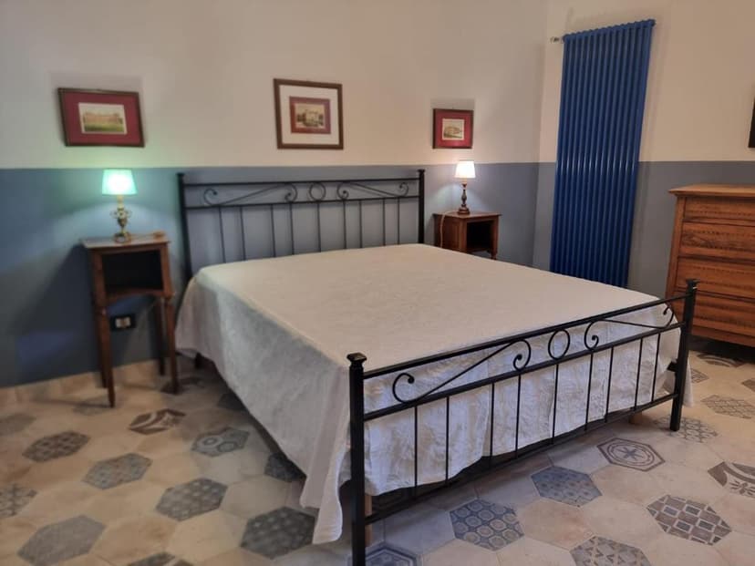 Bedroom with black metal bed, white linens, patterned tile floor, and blue radiator.