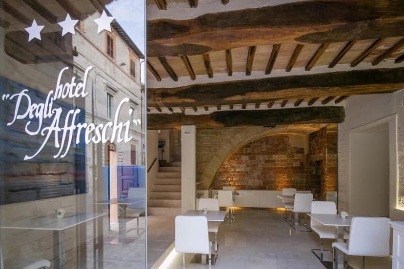 Hotel Degli Affreschi interior with white modern seating, exposed wooden beams, and brick archway.