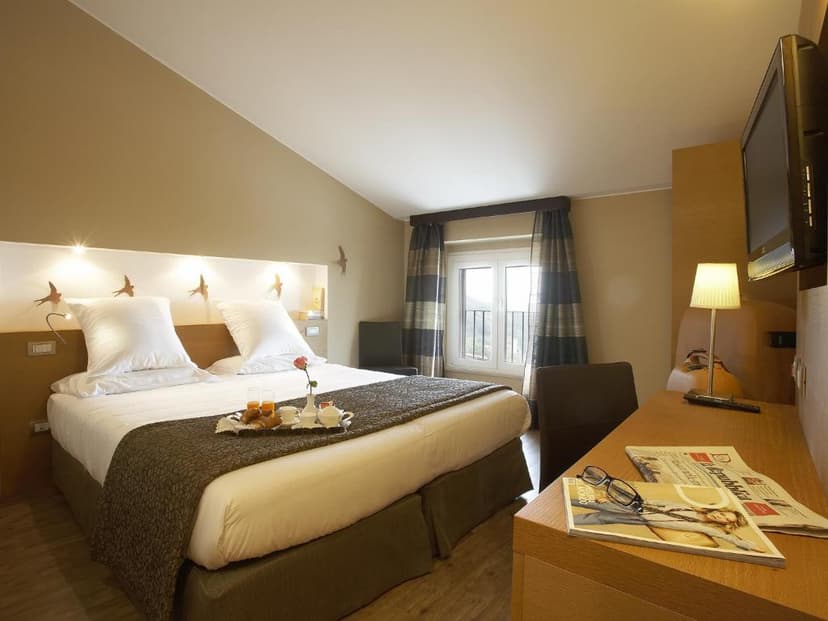 Hotel room with large bed, breakfast tray, and desk featuring a lamp and magazines, Hotel Porta Nuova