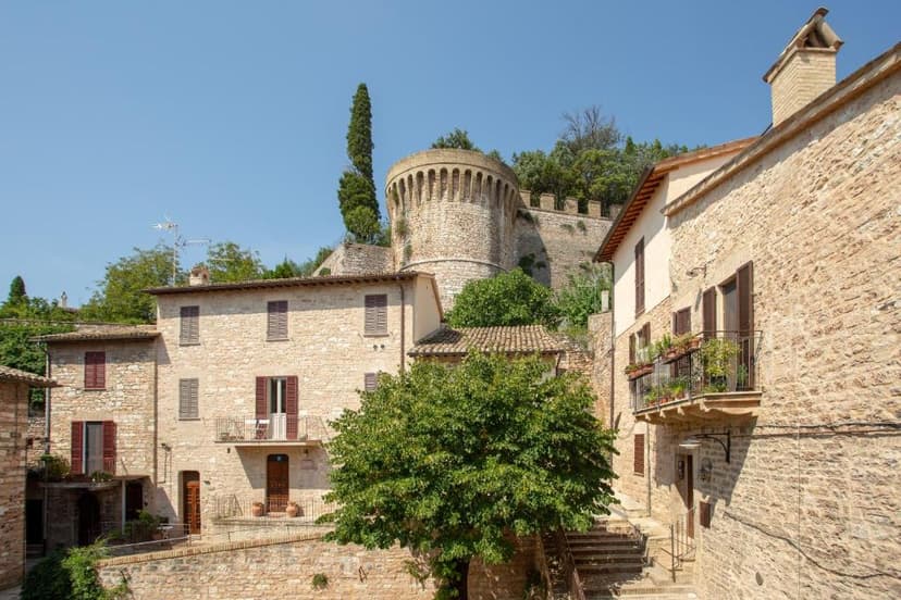 Stone buildings and a medieval fortress tower on a hill in a sunny Italian town.