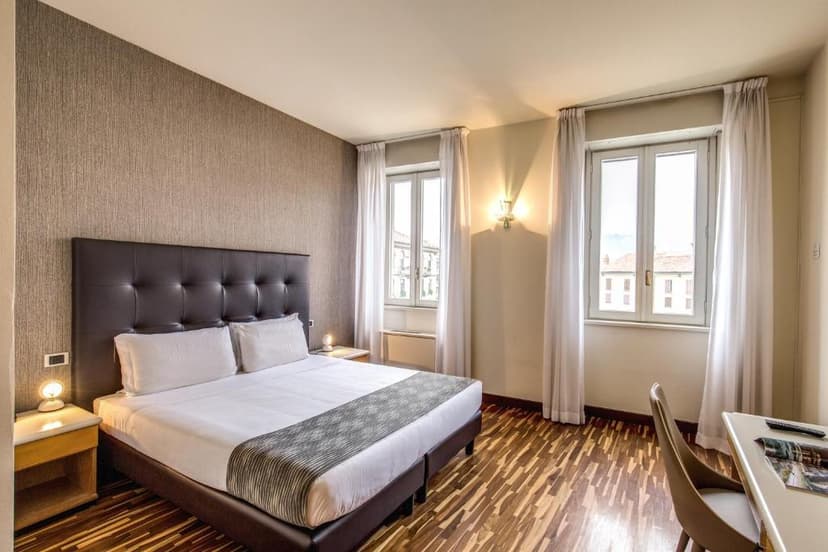 Hotel room in Albergo Firenze with queen bed, wood floor, and city view windows.