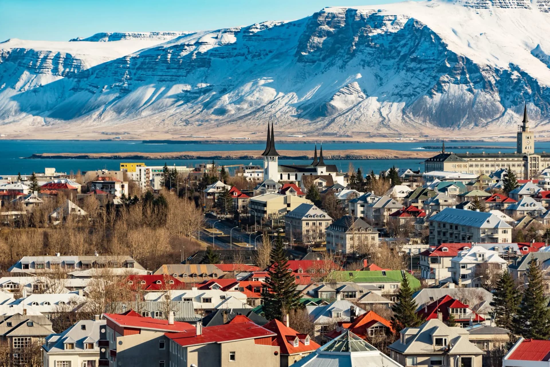 Panoramic view of Reykjavik city with colorful roofs against snow-covered mountains in winter.