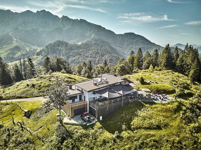 Modern alpine building on grassy hillside with outdoor seating and mountains in background
