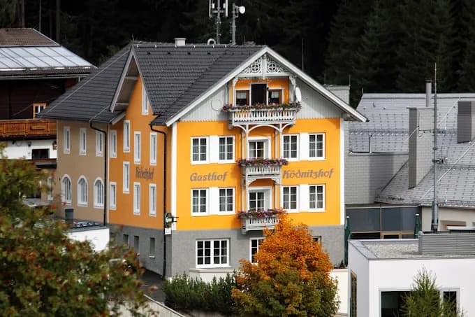 Gasthof Ködnitzhof building with orange facade and balconies against a dark forest background.