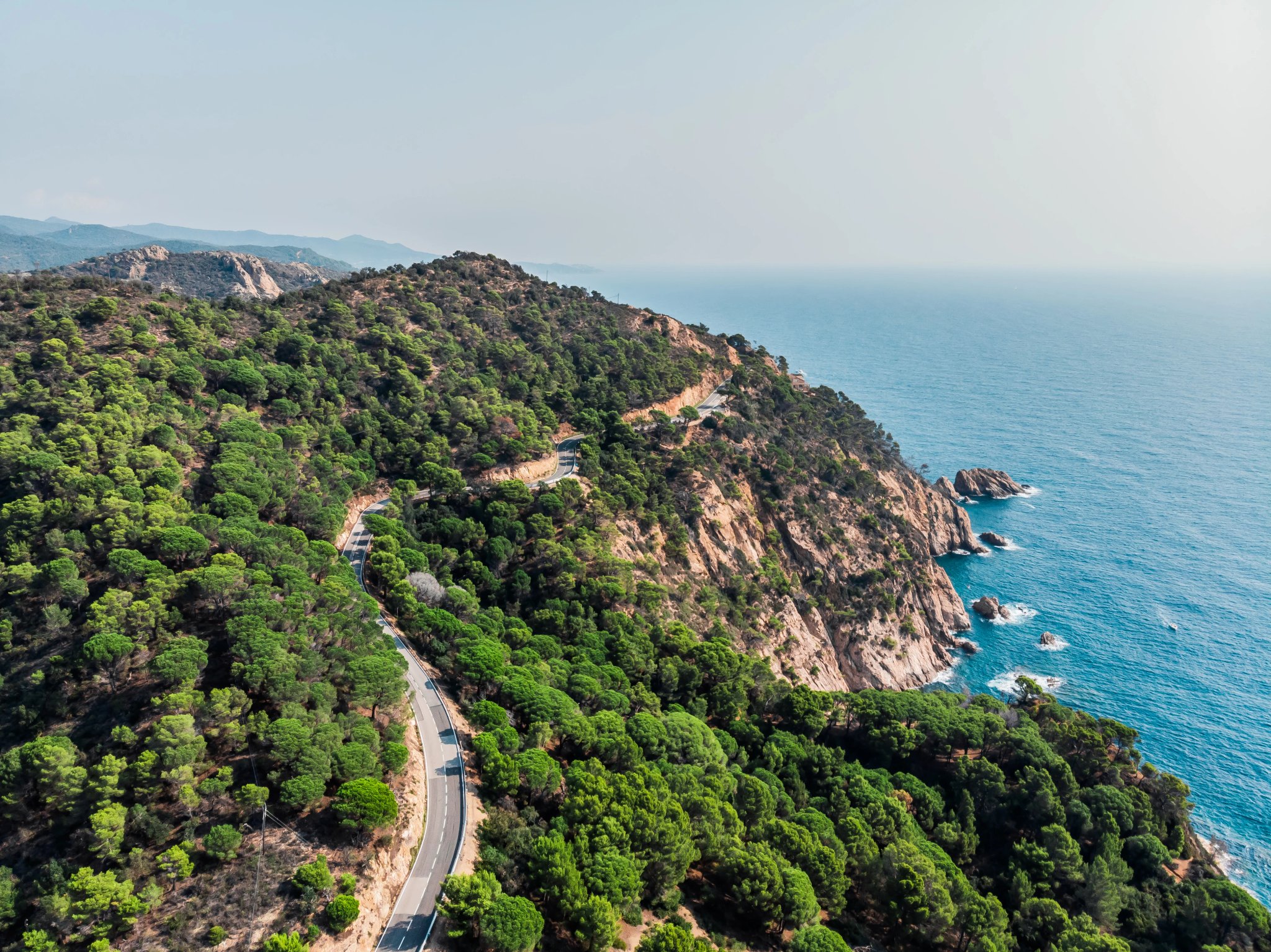 Blick von einer Drohne auf eine Bergstraße in der Stadt Tossa de Mar. Drohnenaufnahme eines Autos, das entlang einer Bergstraße fährt. Der Ferienort Tossa de Mar nahe dem Mittelmeer.