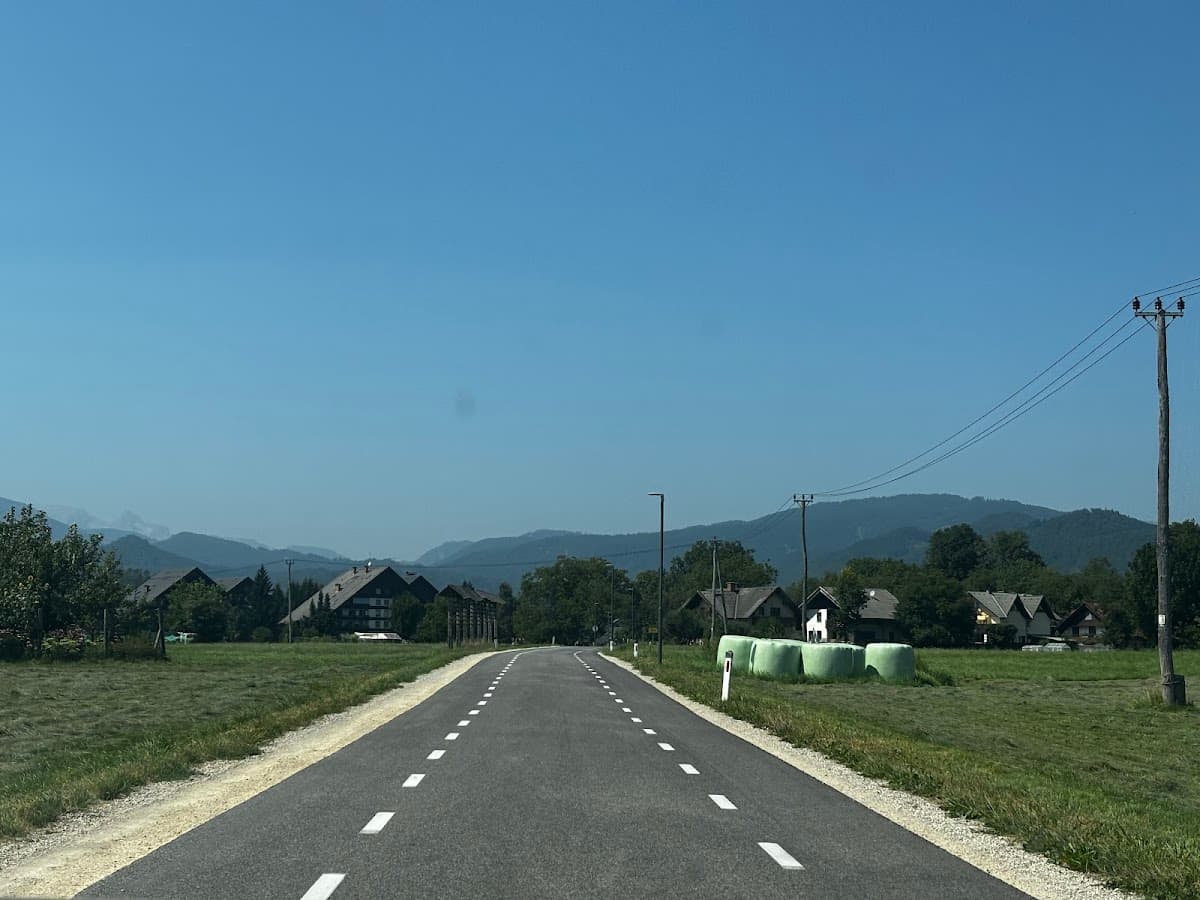 Asphalt road leading toward distant mountains past houses and wrapped hay bales