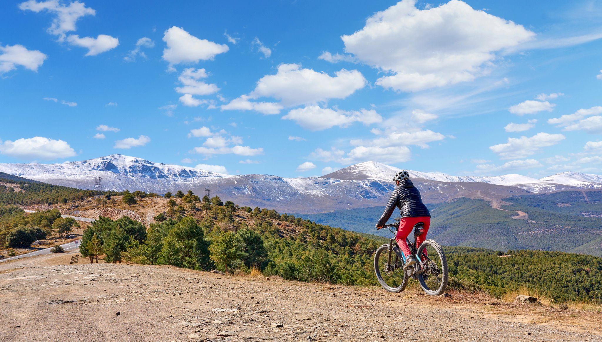 trevlig, aktiv senior kvinna som cyklar med sin elektriska mountainbike under de snötäckta bergen i den spanska Sierra Nevada, nära Granada, Andalusien, Spanien