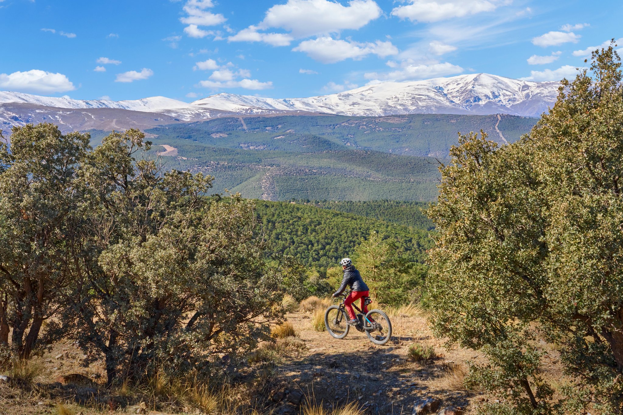 trevlig, aktiv senior kvinna som cyklar med sin elektriska mountainbike under de snötäckta bergen i den spanska Sierra Nevada, nära Granada, Andalusien, Spanien