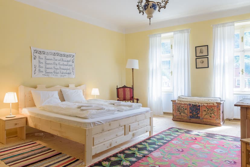 Bright bedroom with light wood bed, colorful rug, and painted chest in Transylvania room.