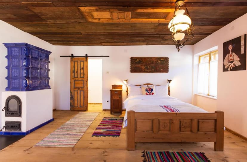 Rustic bedroom with wooden ceiling, blue tiled stove, and carved wooden bed frame.