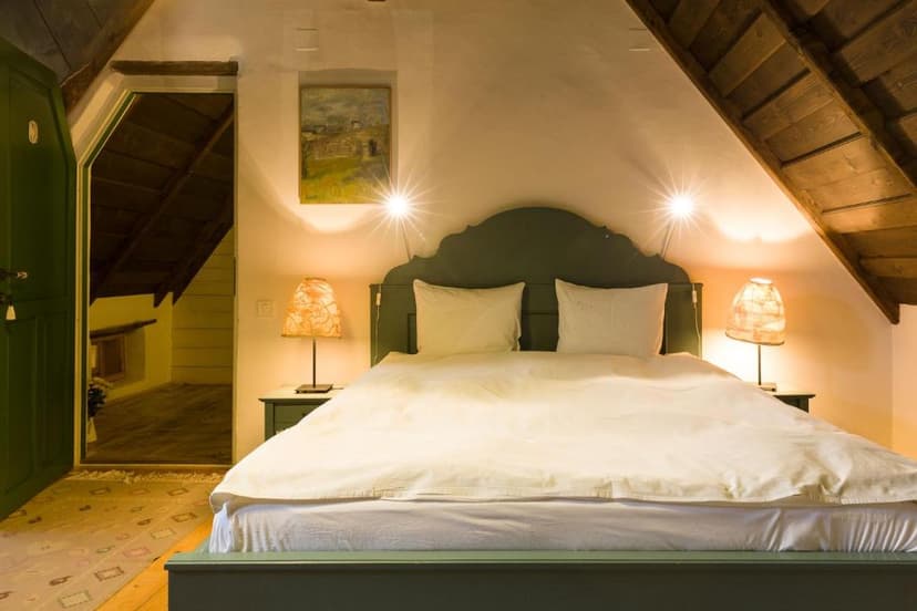 Cozy attic bedroom with green bed frame, white bedding, and exposed wooden ceiling beams in Viscri.