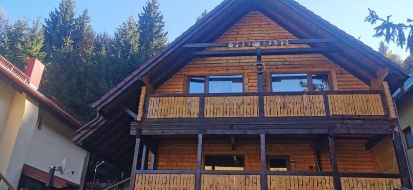 Wooden log cabin with balconies nestled against a backdrop of dense evergreen trees.