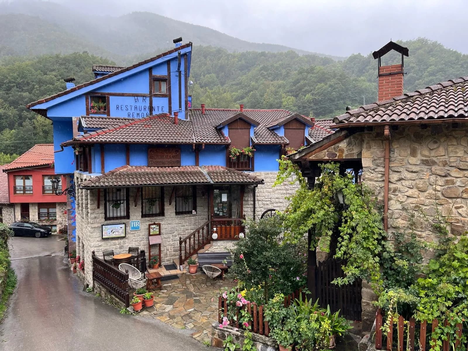 Stone and blue buildings in Espinama village with lush green mountains in the mist.