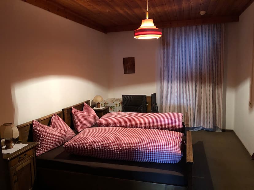Bedroom with wooden ceiling, red gingham bedding, and hanging lamp at Rifugio Prato Piazza.