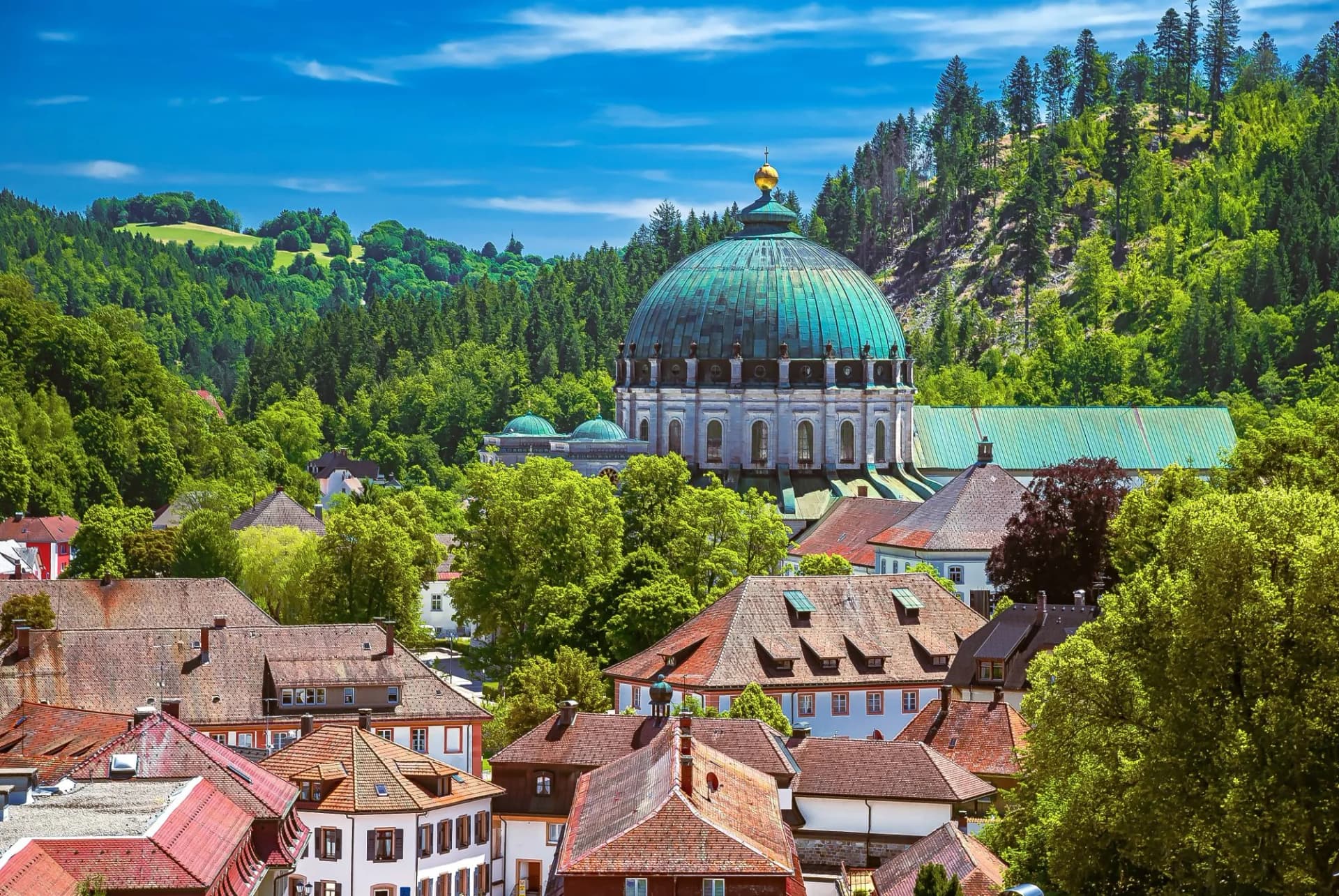 Baroque abbey dome in Sankt Blasien surrounded by dense green forest and red-roofed town buildings.