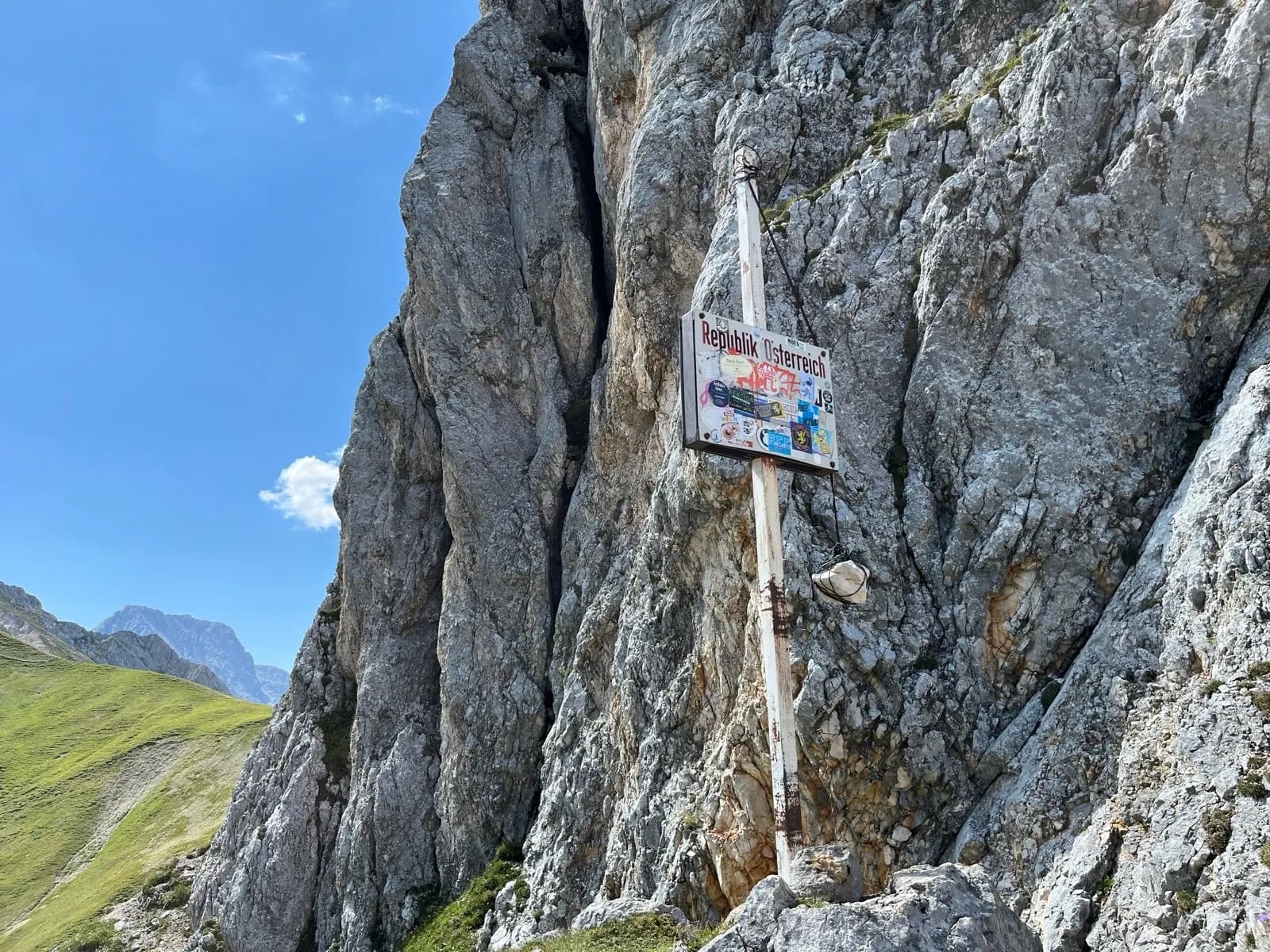 Boundary marker sign for Republik Österreich attached to a massive rock face on a sunny day.