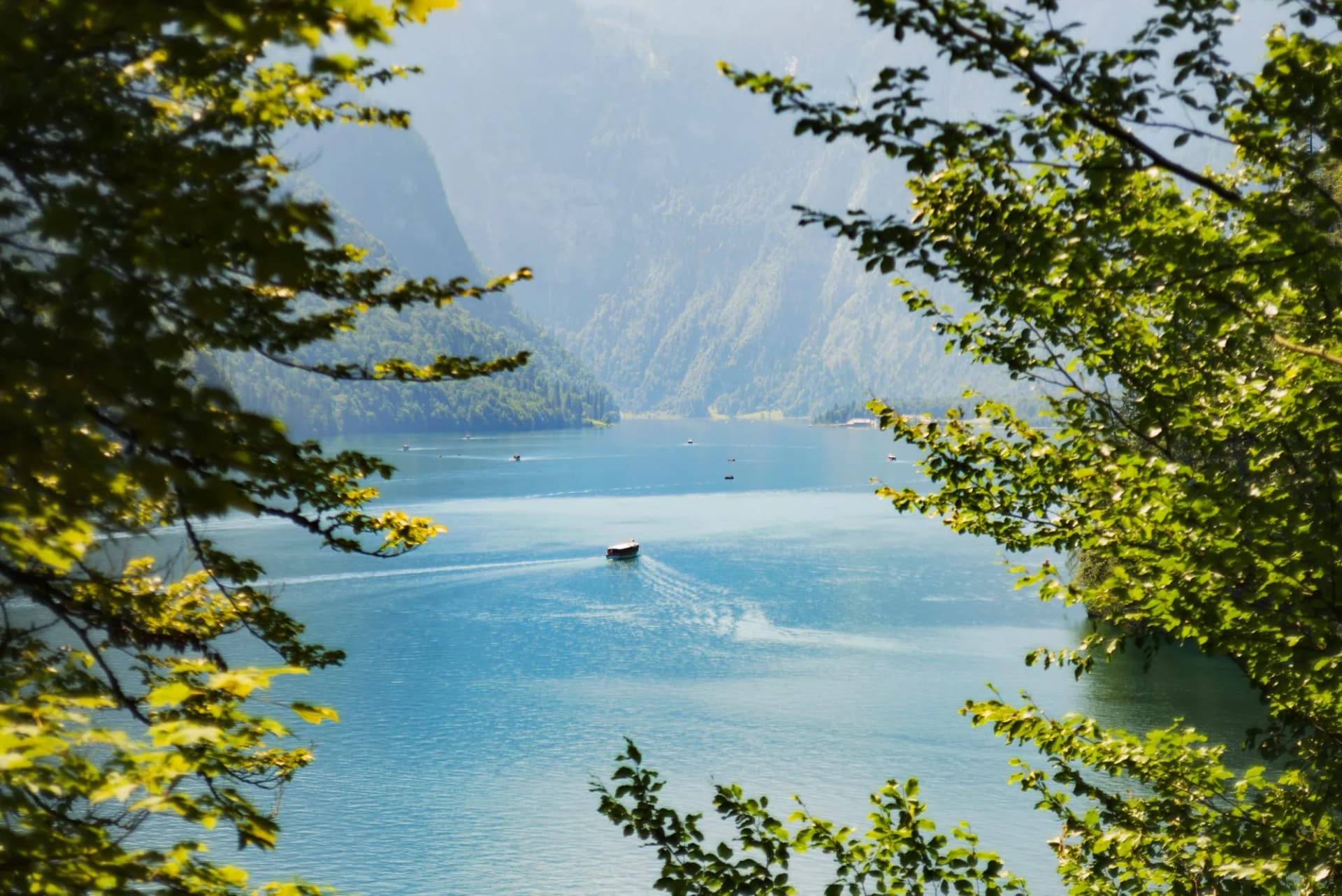 Boat on bright blue alpine lake framed by green summer foliage with steep mountains.
