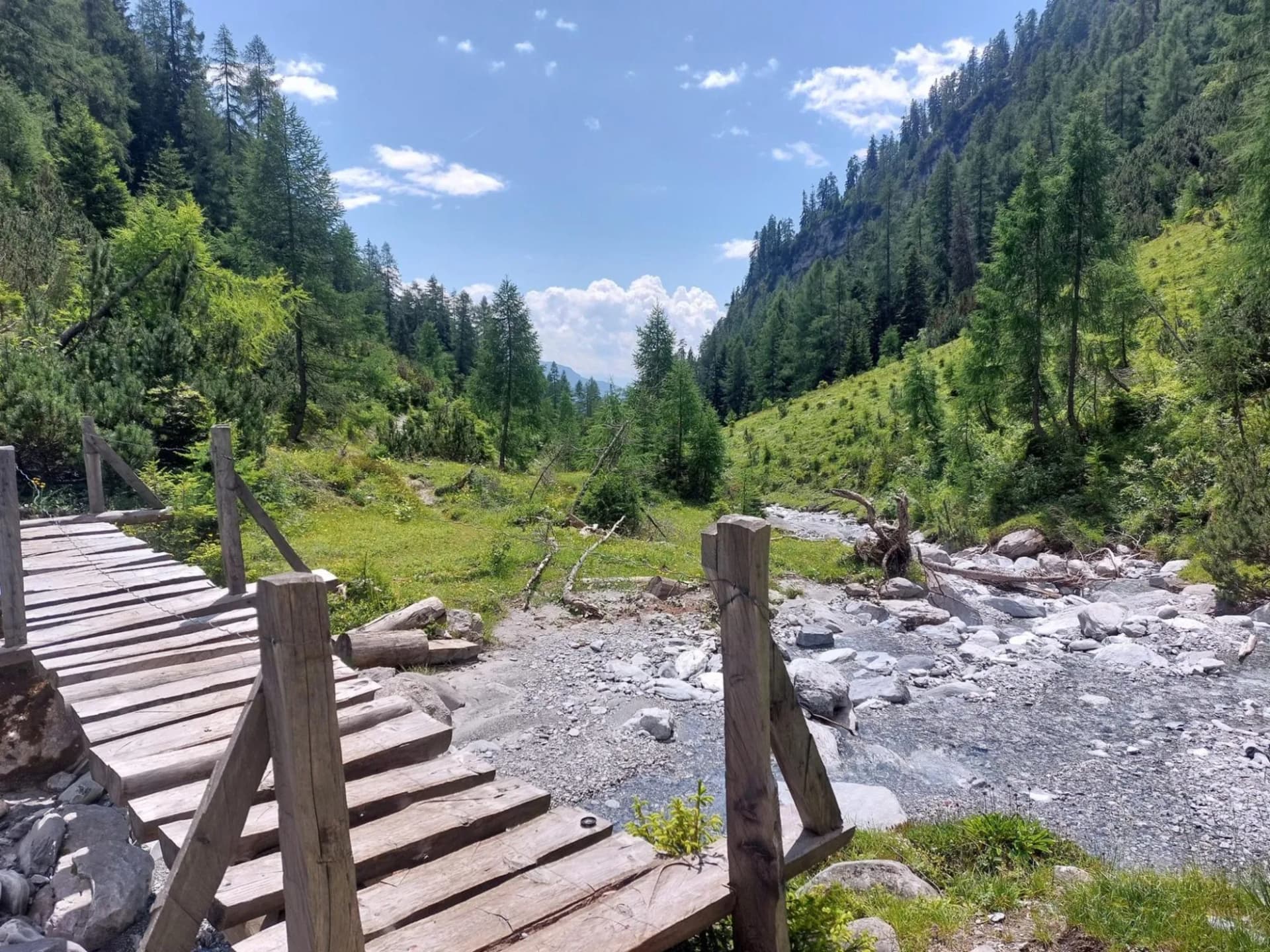 Wooden footbridge over a rocky stream in a lush green mountain valley hike.