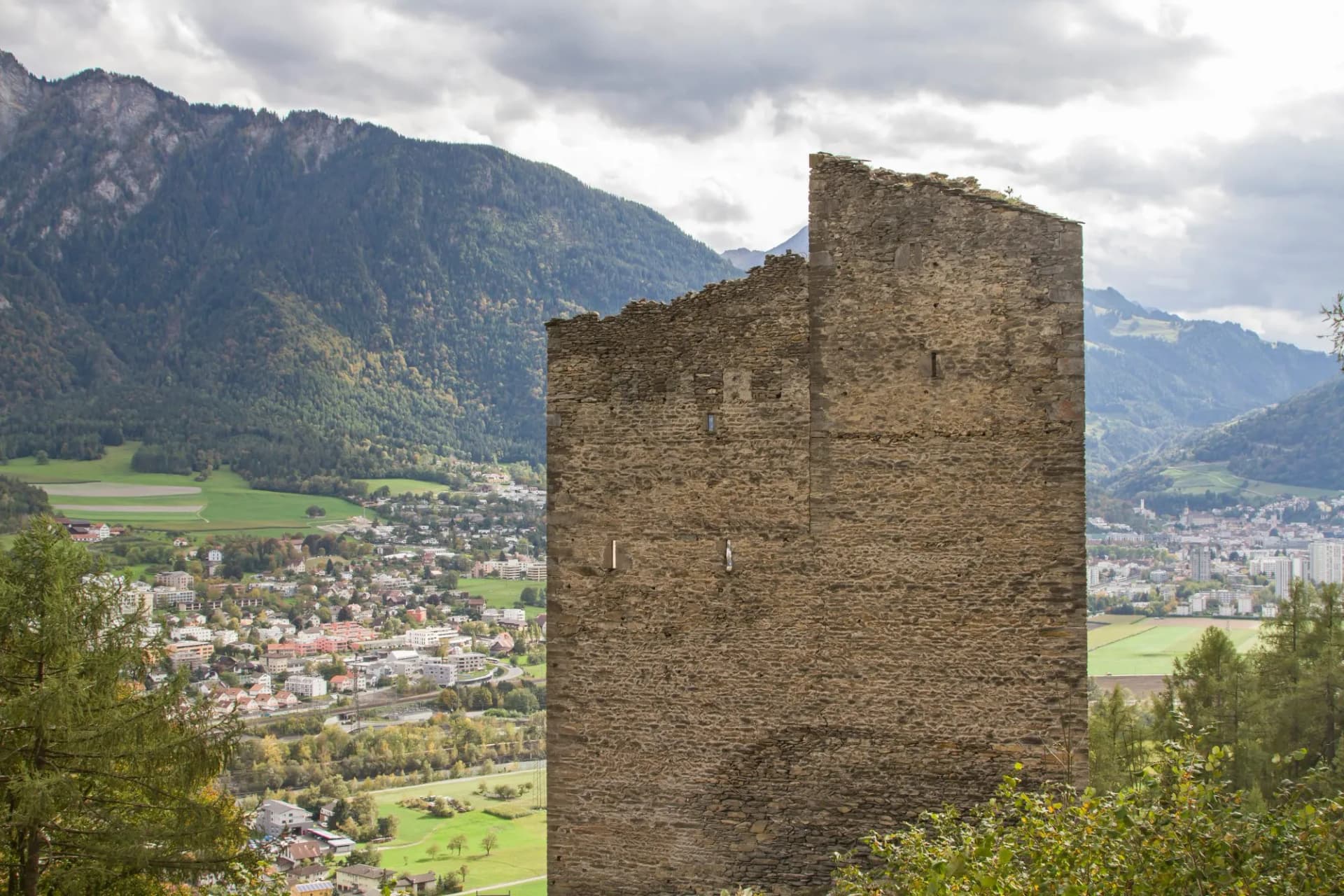 Ruin of Haldenstein Castle tower overlooking a valley town and forested mountains.