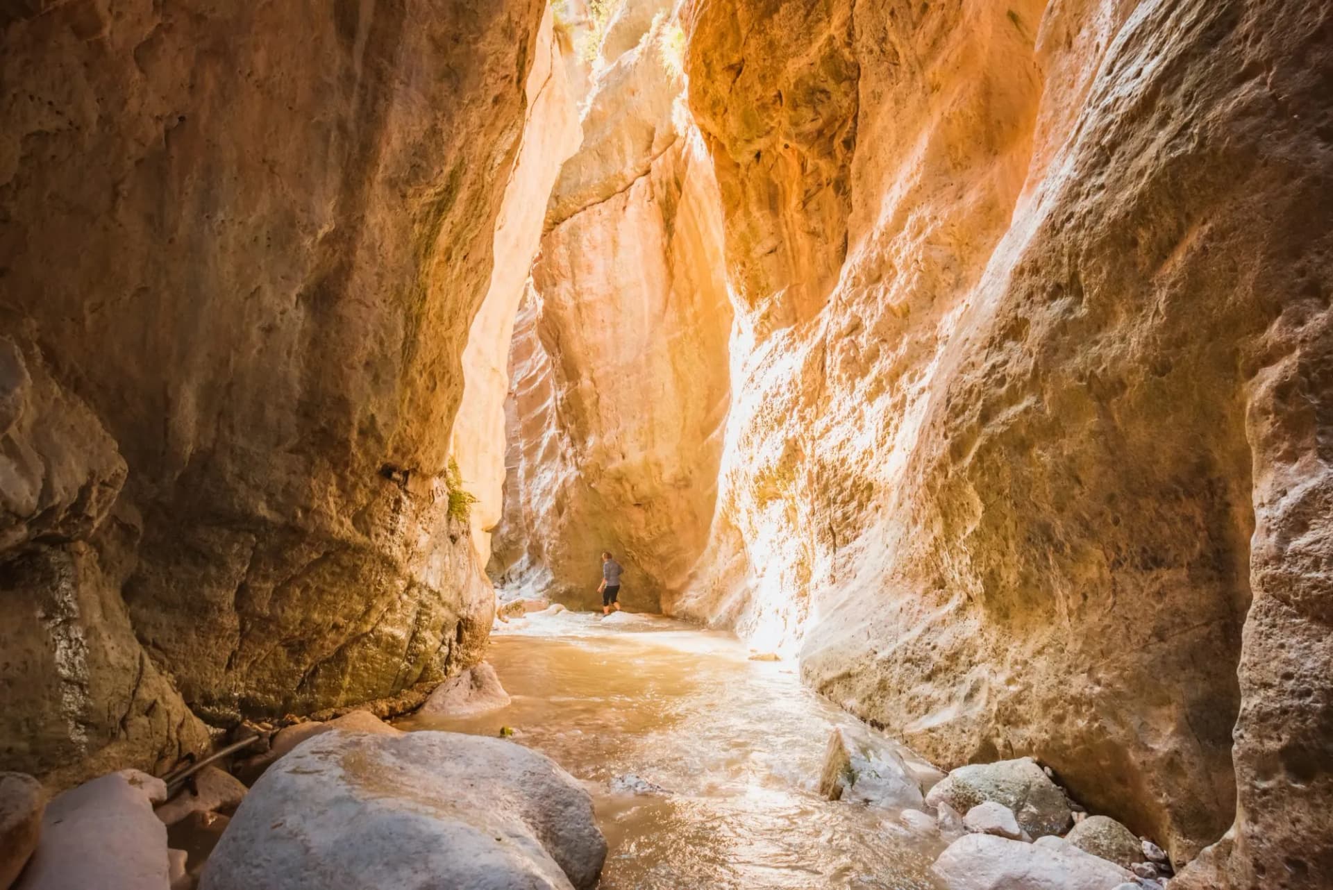 Hiker wading through shallow water in the narrow, sunlit Avakas Gorge canyon.