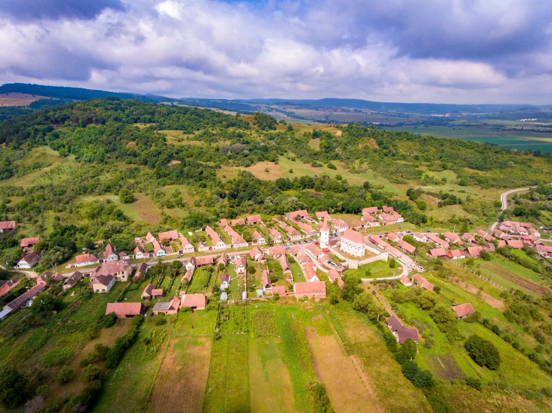 Aerial view of Cloasterf village with terracotta roofs, green hills, and cloudy sky.