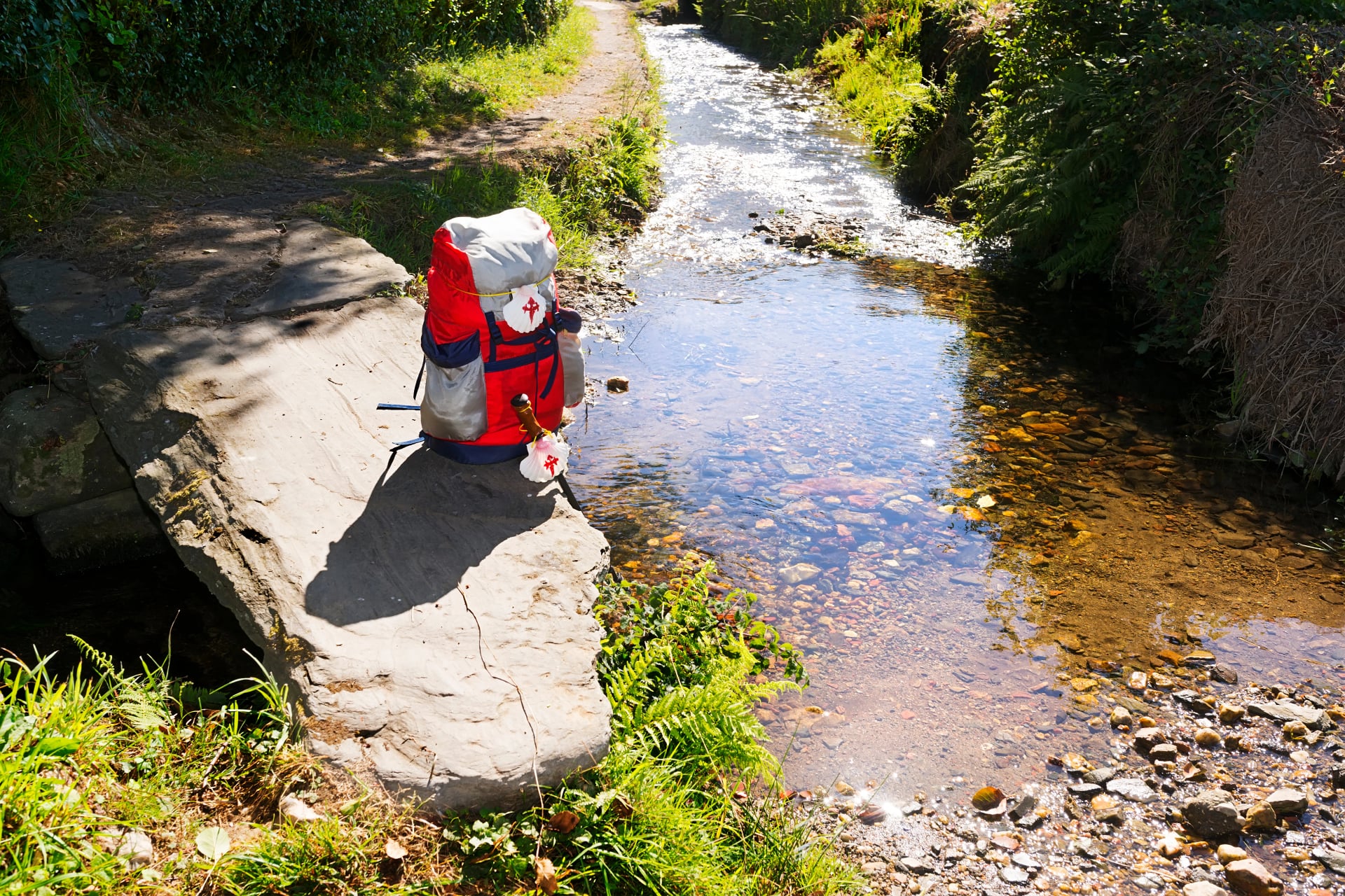 scallop shell in backpack and cane near the river , Camino de Santiago to Compostela , english way near Pontedeume