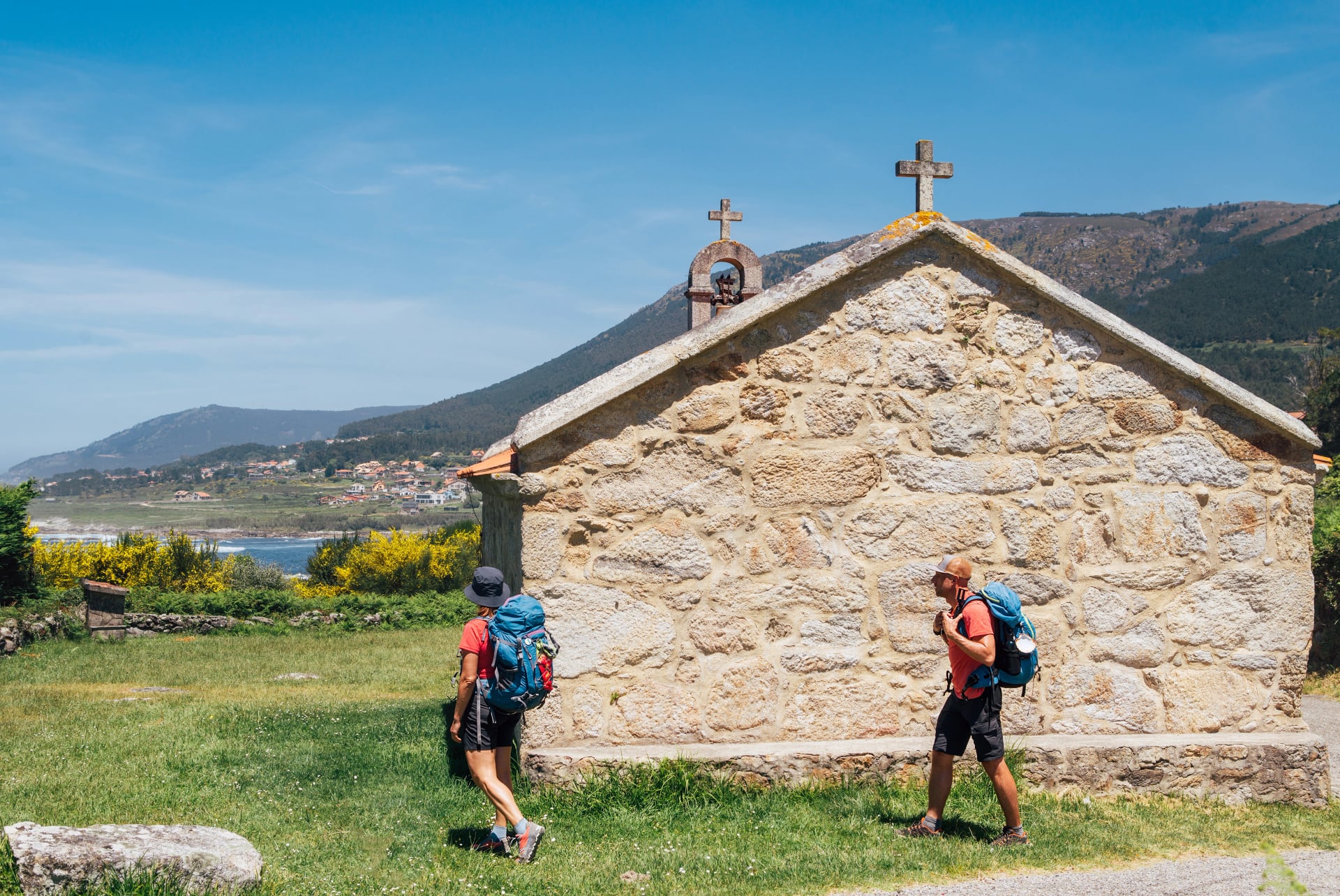 Couple of pilgrims with backpacks walking next to old church on Camino Portuguese Way, inspiring walk on famous Camino de Santiago. Travel, pilgrimage, lifestyle, architecture