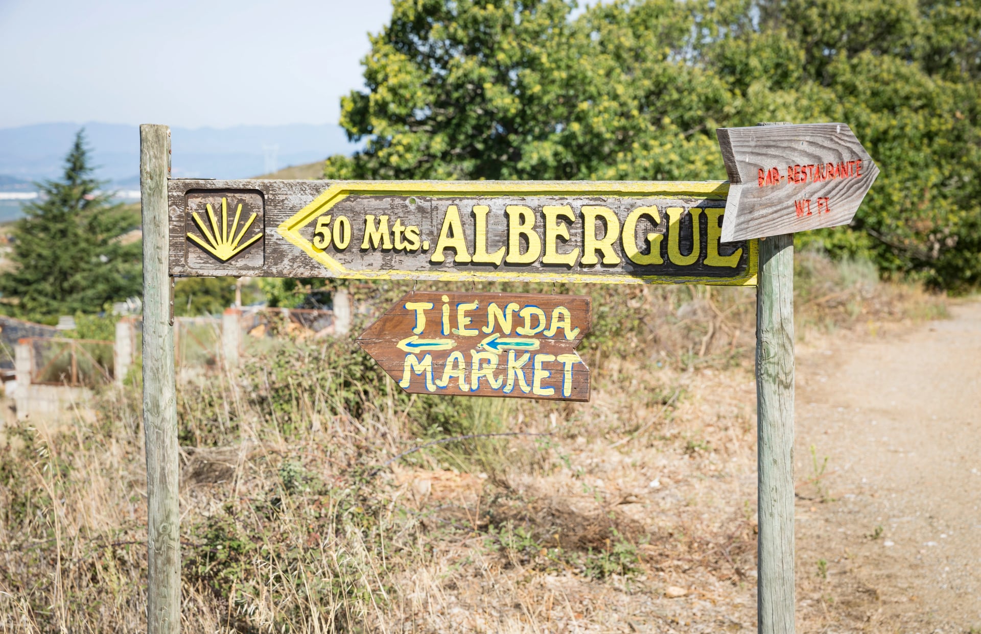 wooden signpost pointing the way to an Albergue (hostel) and a yellow shell as a symbol of the way to Santiago