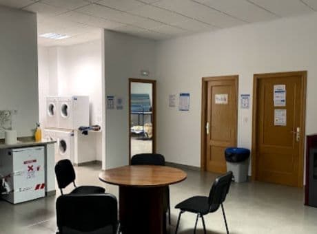 Laundry area with washing machines, round table, and black chairs inside Vilamartín de Valdeorras Municipal Hostel.