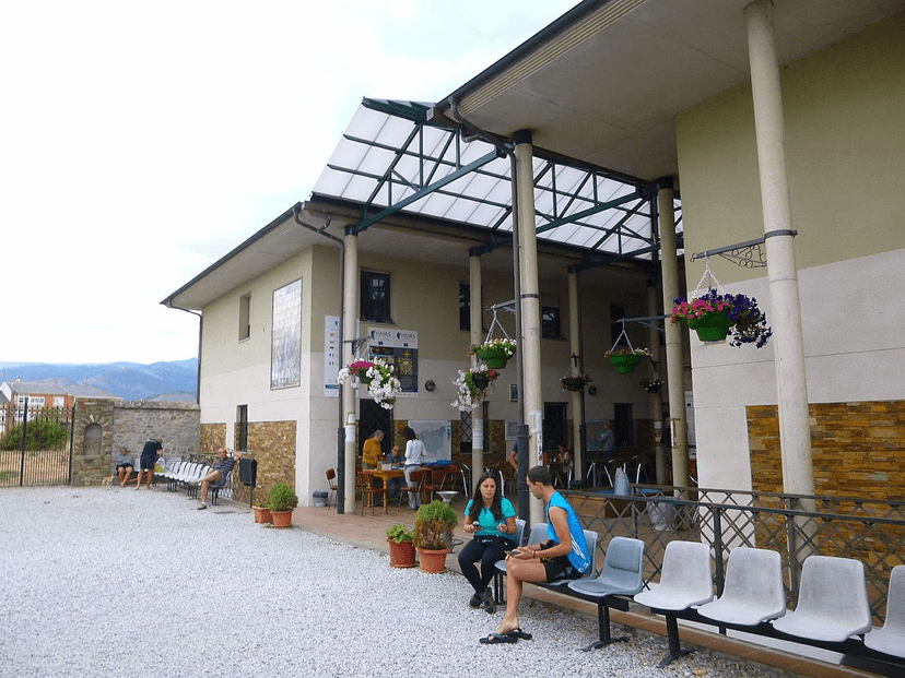 Pilgrims resting outside Albergue de peregrinos San Nicolás de Flüe in Ponferrada, with mountains in the background.