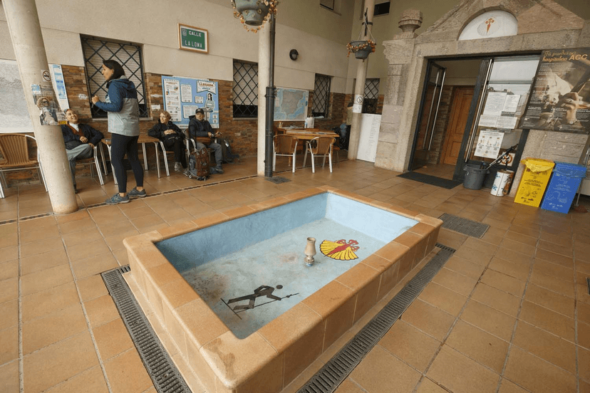 Pilgrims resting near a dry fountain with scallop shell symbol at Albergue San Nicolás de Fluee, Ponferrada.