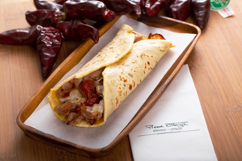 Savory crepe filled with meat and sun-dried tomatoes on a wooden tray with dried chili peppers.
