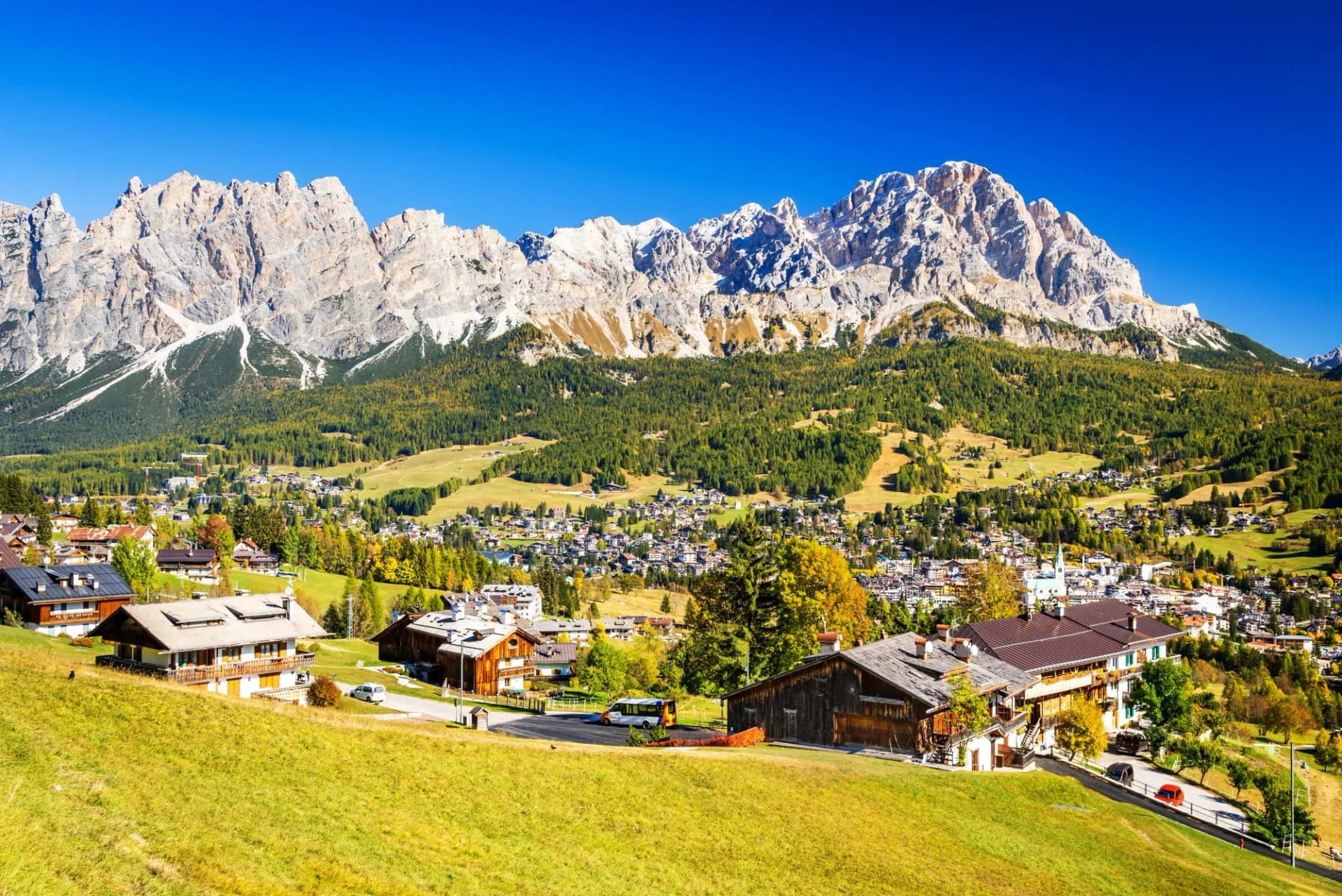 Cortina d'Ampezzo town nestled below rugged Dolomite mountains under clear blue sky.