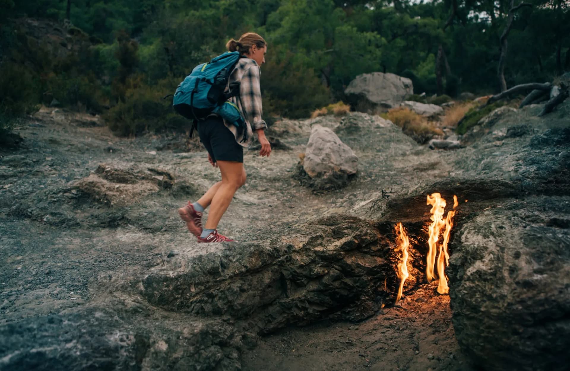 Backpacker woman hiking alone along fires of Yanartas at night on Mount Chimaera on popular hiking Lycian Way (Likya Yolu) in Antalya Province, Turkey. Unique Geothermal phenomenon.