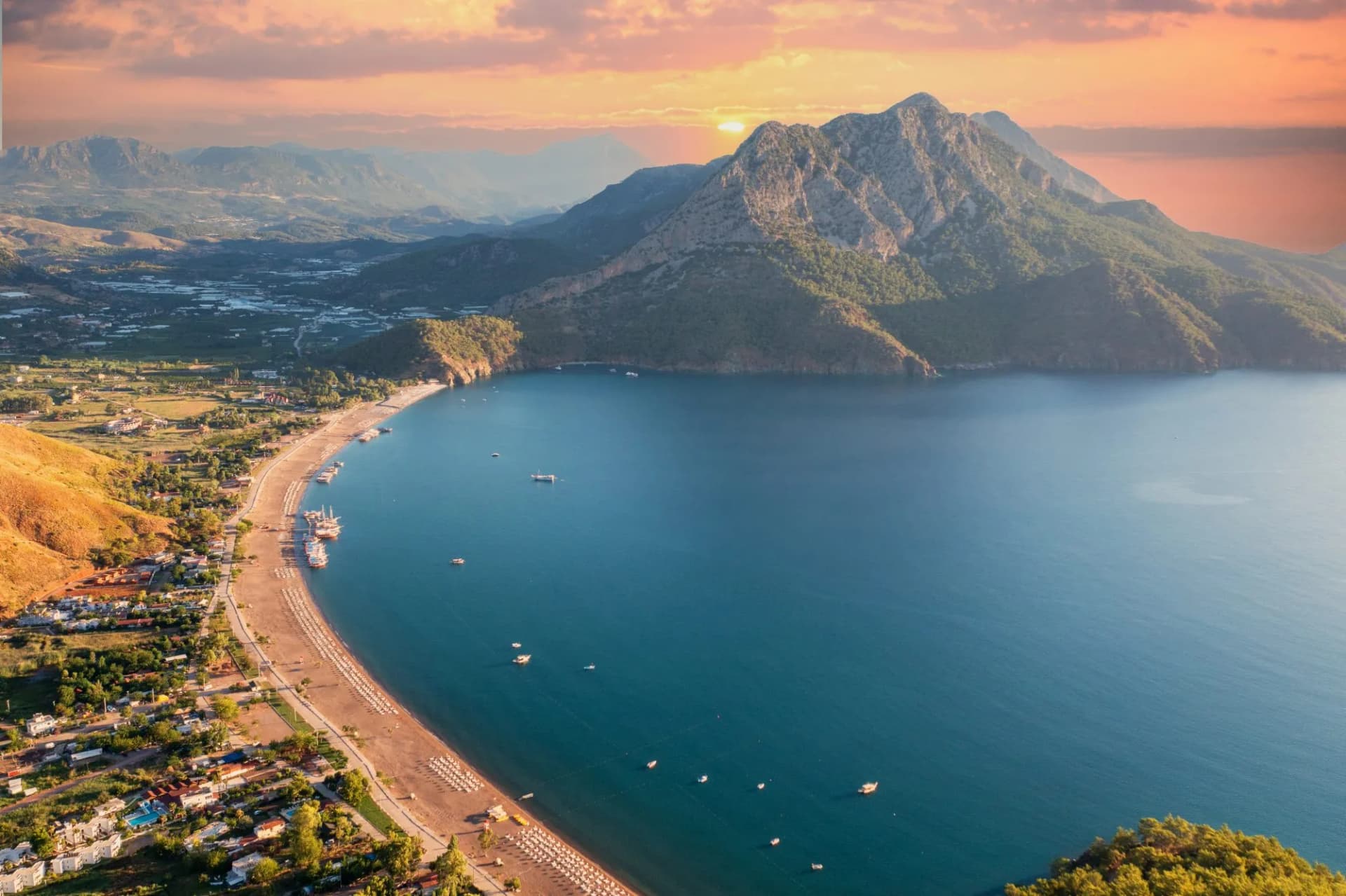 Coastal bay with beach, boats, and mountains at sunset in Adrasan, Turkey.