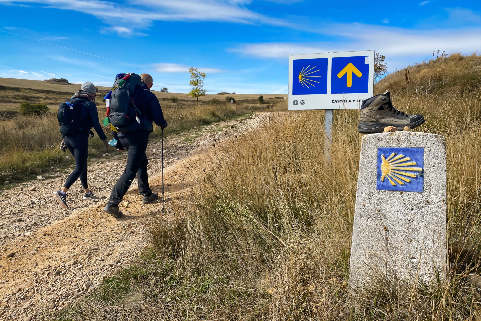 Pilgrims Walking past Way Marker Signs with Yellow Arrows and Scallop Shells on the Meseta outside Rabé de las Calzadas on the Way of St James - Camino de Santiago