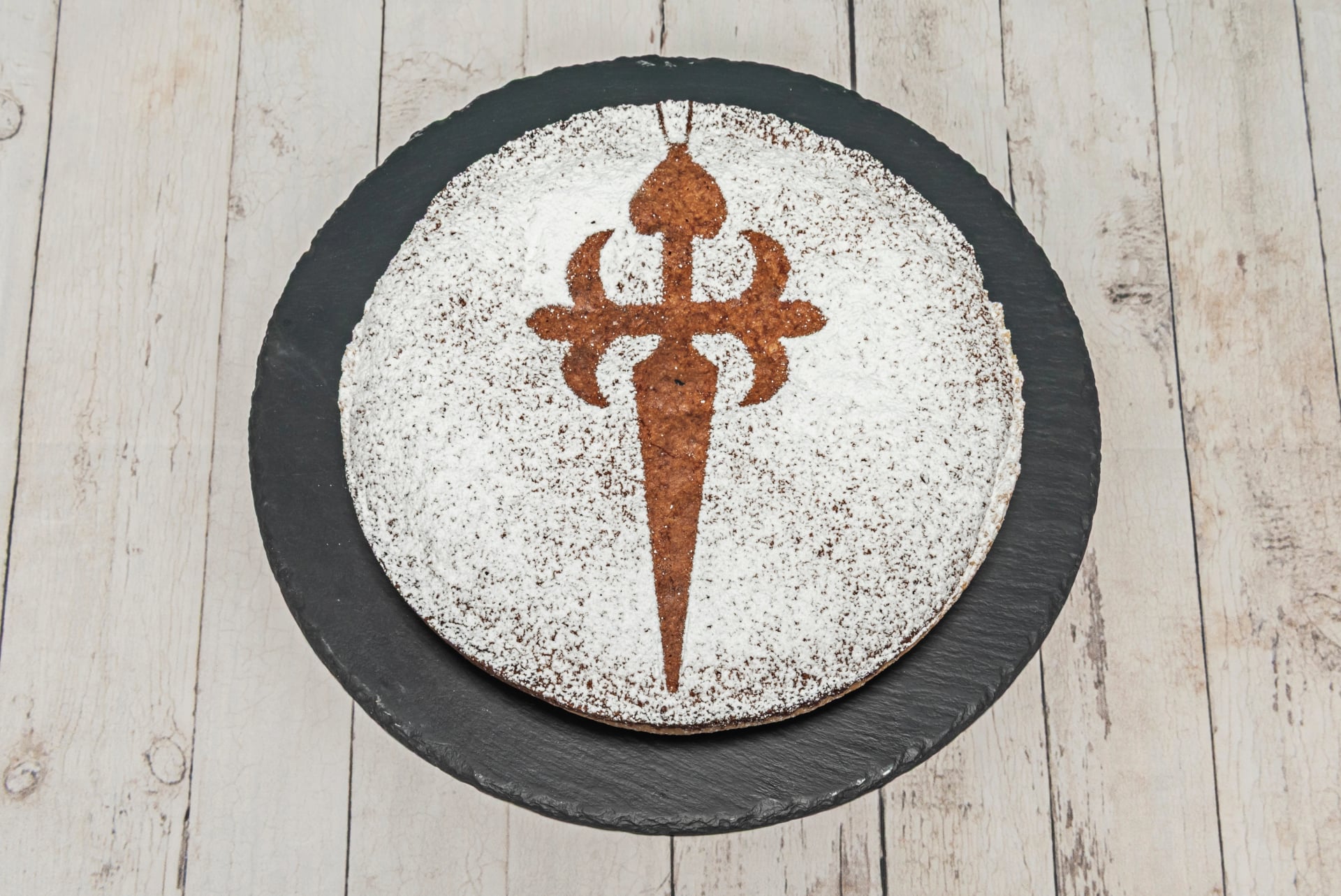 Individuel portion af Tarta de Santiago dekoreret med det ikoniske broderede kors i flormelis, på en galicisk kunstnerisk keramisk tallerken