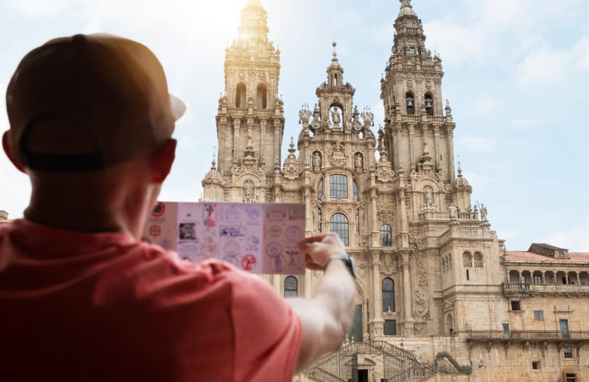Pilgrim man checking his Pilgrim Credential passport with stamps on Obradoiro square in Santiago de Compostela, Spain with Santiago de Compostela Cathedral — famous Camino de Santiago finish point
