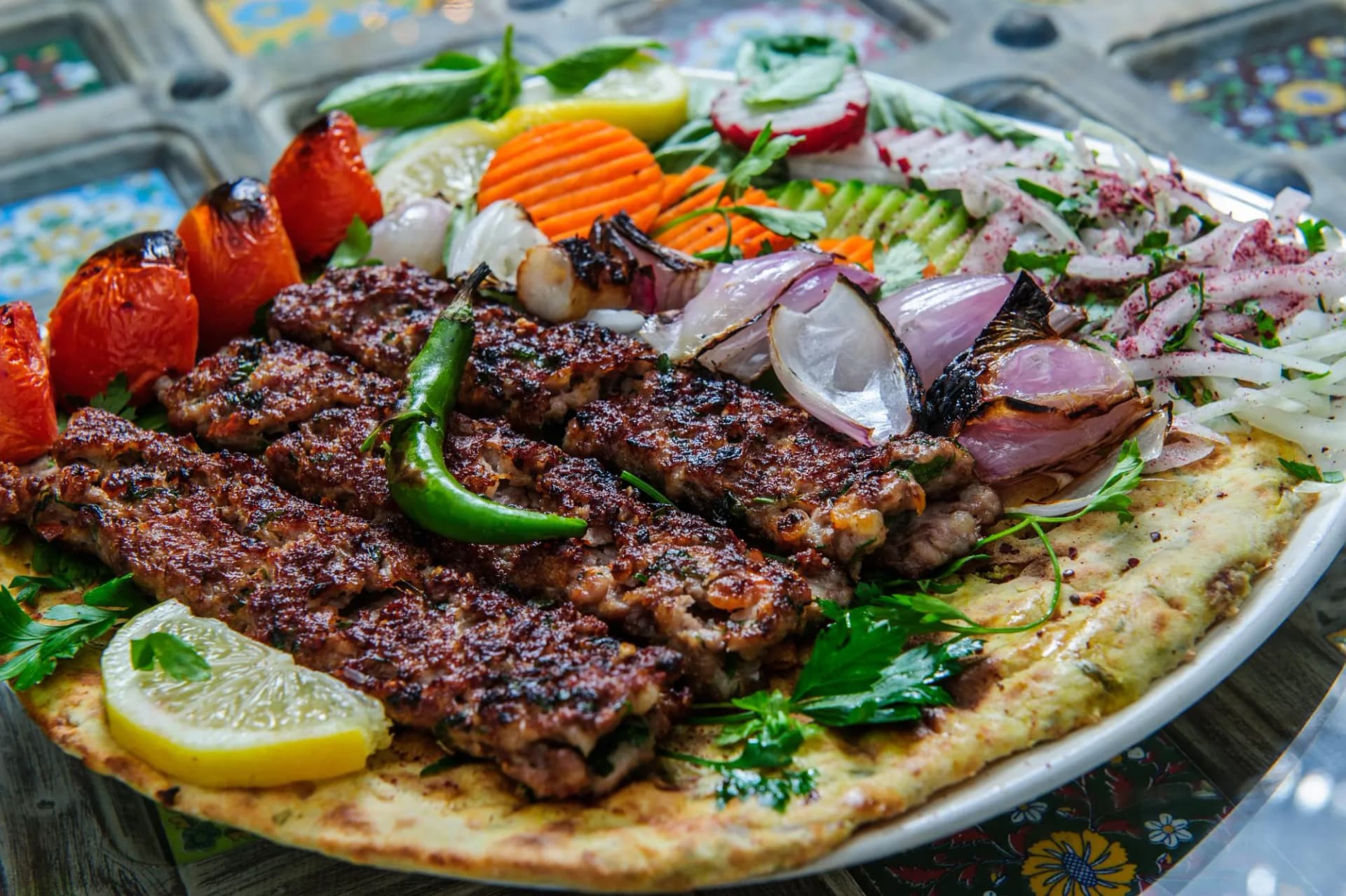 Grilled kebab served on flatbread with grilled tomatoes, onions, lemon, and fresh vegetables.