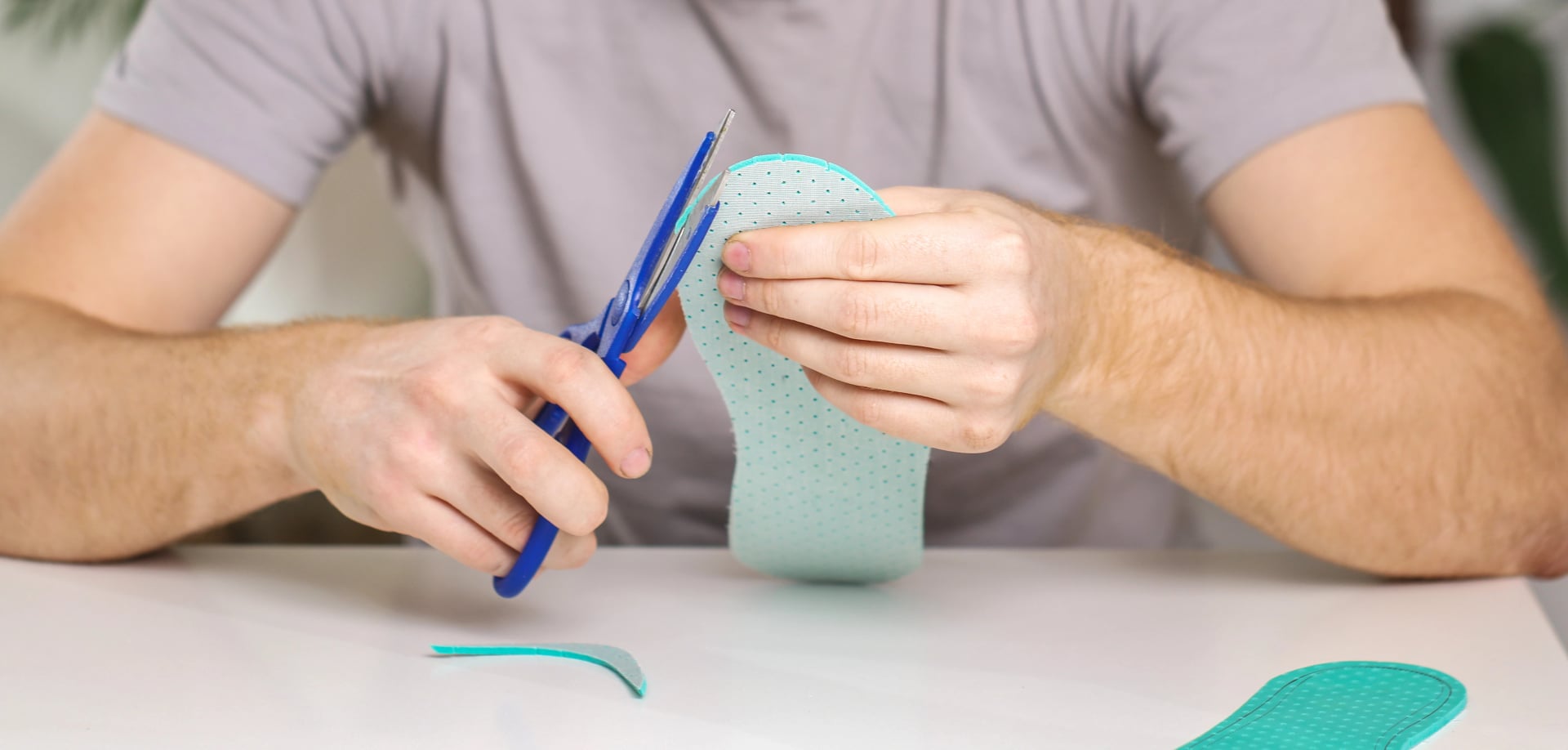 Man cuts out new shoe insoles with scissors to fit his foot size.