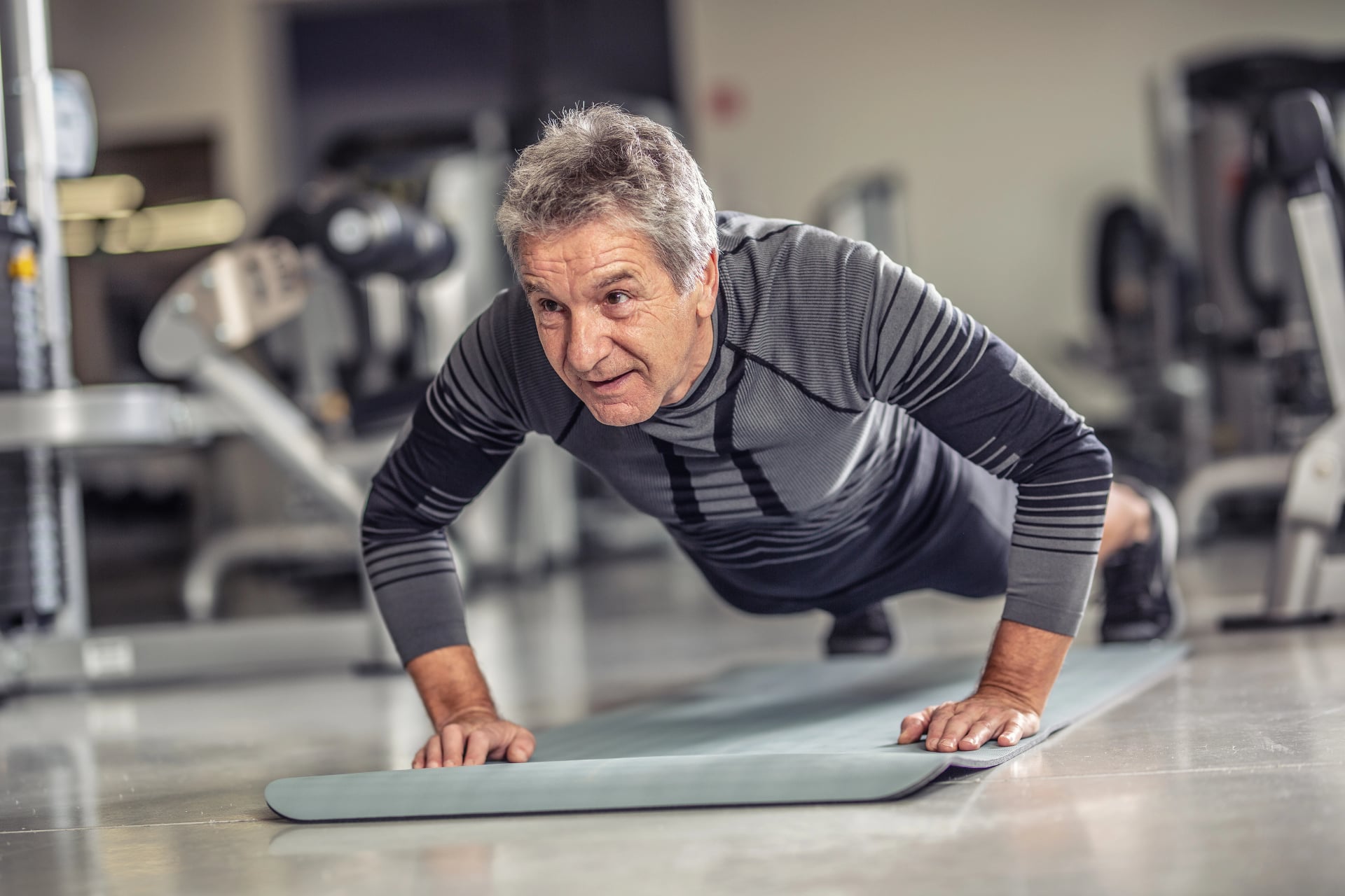 Senior male stays fit by doing pushups on a mat inside the fitness center