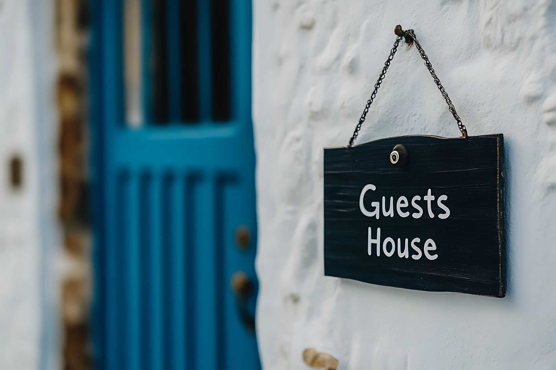 Charming guesthouse sign hanging on a white wall next to a bright blue door. Inviting entrance to a cozy accommodation. Hospitality is key.