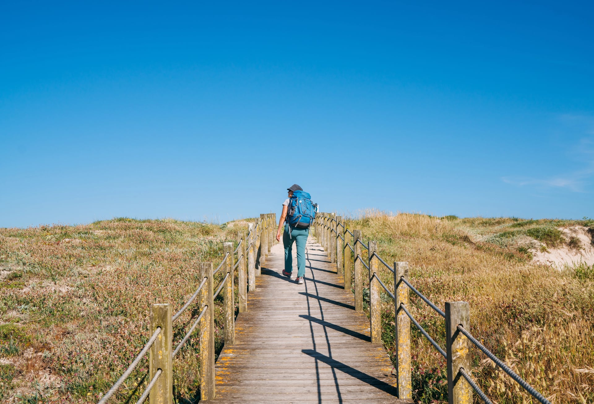 Middle-aged woman with backpack walking in Portugal on the Camino Portuguese — a popular pilgrimage route to Santiago de Compostela. Concept of active lifestyle, travel, and happiness.