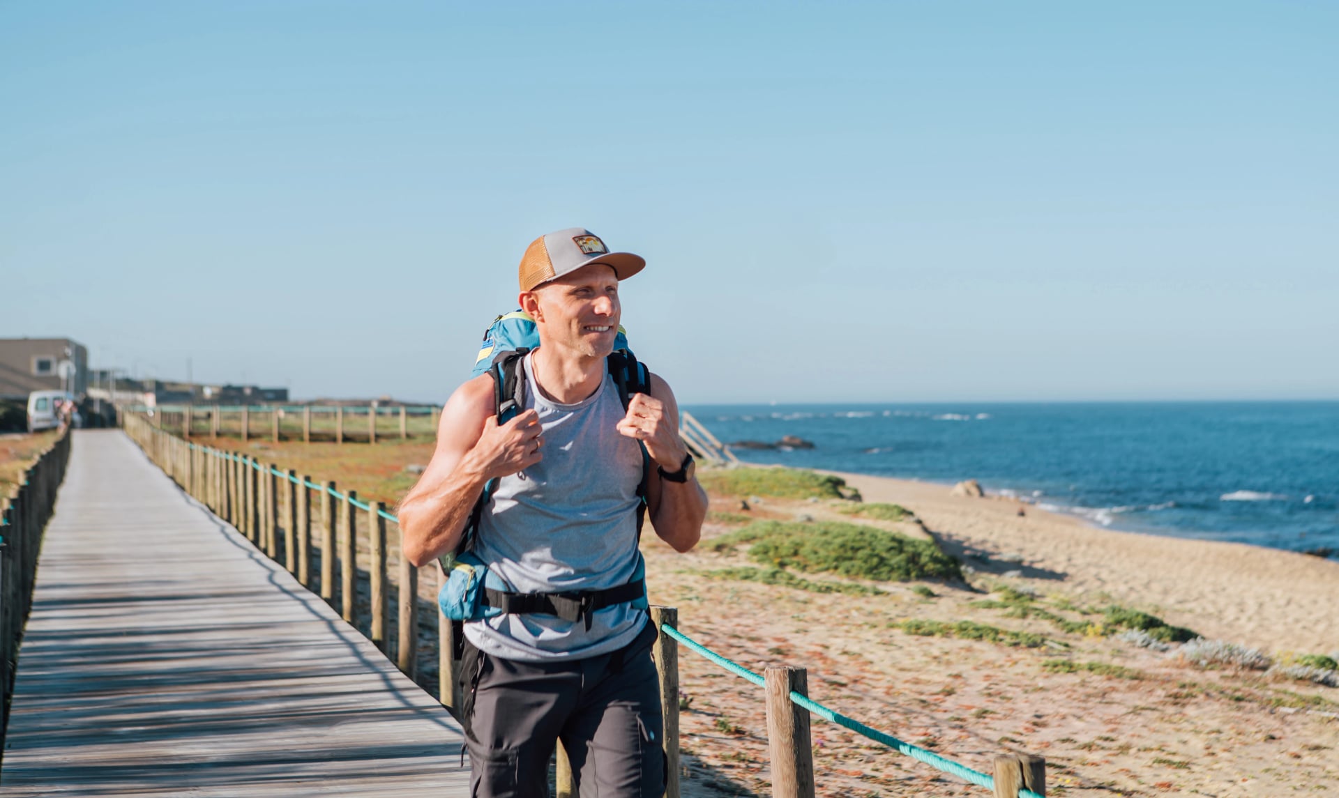 Lonely backpacker smiling man walking by sandy Portugese beach in morning. Path leading by wooden passadicos - boardwalks along the ocean coast. Shot during Camino Portuguese popular pilgrimage route