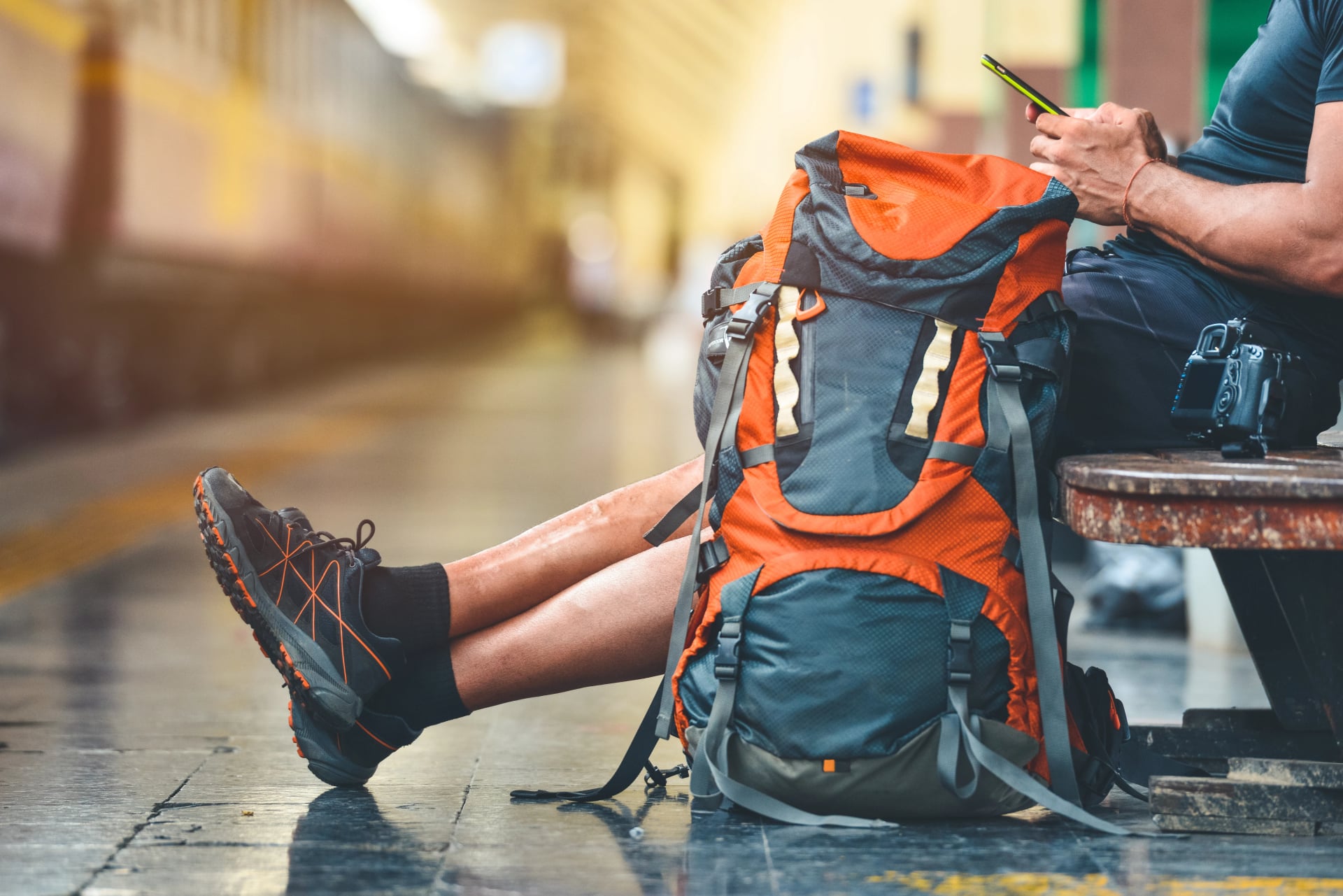 Tourist man with a backpack in the train station holding a smart phone. A camera on the bench. Digital nomad traveler concept