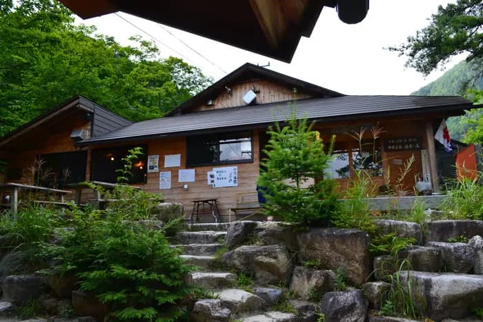 Wooden lodge entrance with stone steps surrounded by lush green foliage, Nakabusa Onsen.
